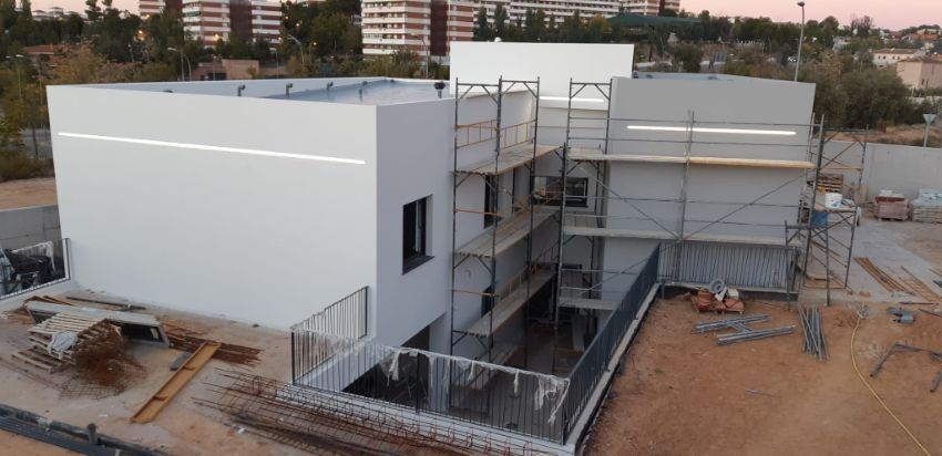 Edificio moderno de dos pisos en construcción, exterior blanco, andamios, nivel del suelo al aire libre, lote de arena.