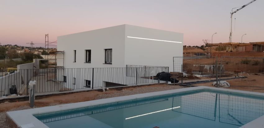 Una casa moderna blanca en construcción, con piscina en el frente.