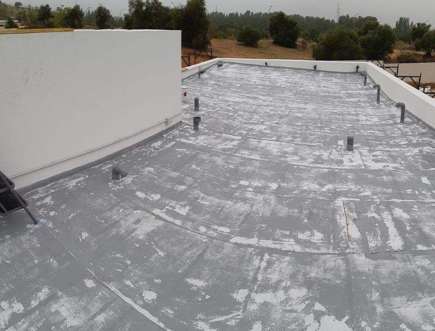 Techo plano gris con daños en la pintura blanca, varias tuberías y un muro bajo.