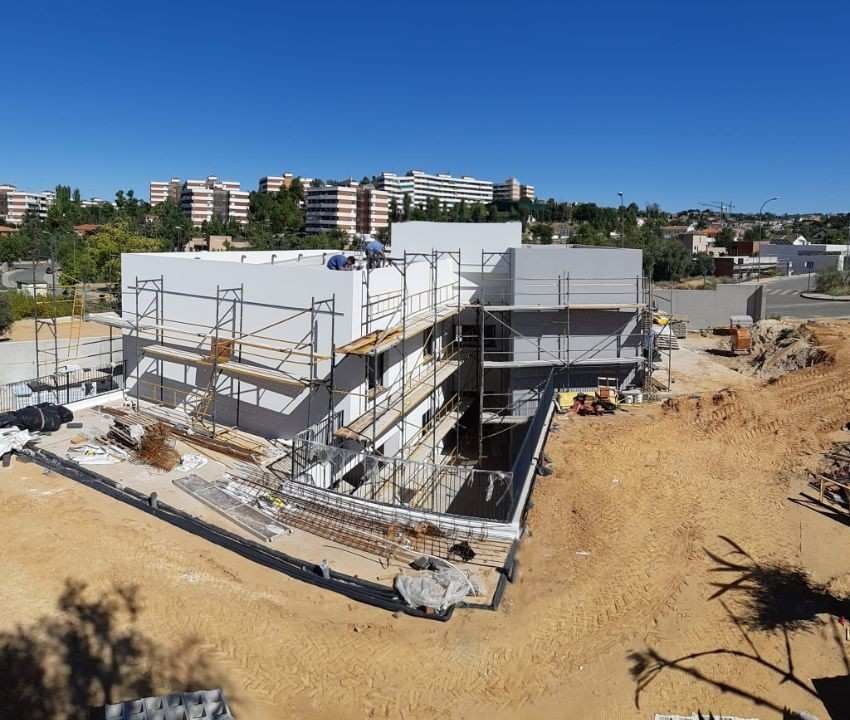 Sitio de construcción con andamios alrededor de un edificio de color claro bajo un cielo azul claro.