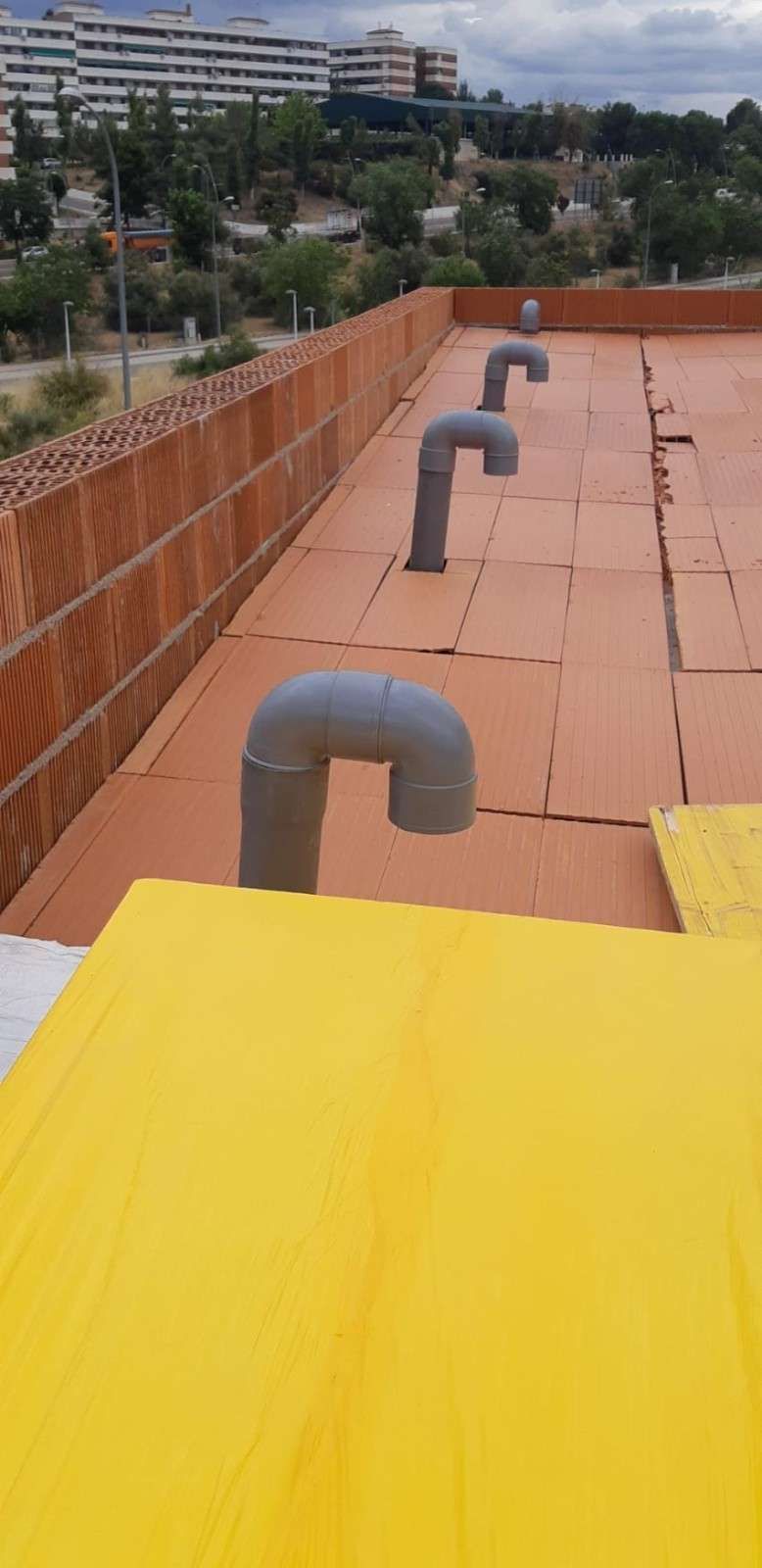 Techo con aislamiento naranja y tuberías curvas grises. Una lona amarilla cubre parte del techo.