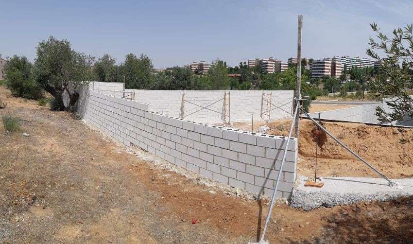 Construcción de muros de bloques de hormigón en una ladera con edificios al fondo.