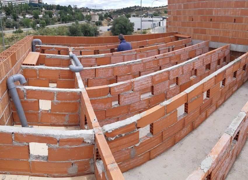 Estructura de ladrillo en construcción, posiblemente para una fuente de agua, con tuberías y una persona trabajando.
