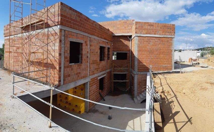 Construcción de un edificio de ladrillo de dos pisos, andamios, ventanas abiertas, cielo brillante y entorno al aire libre.