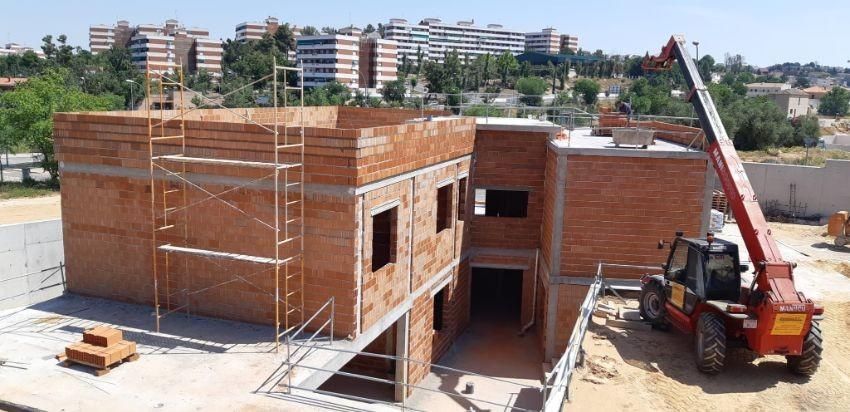 Edificio en construcción con paredes de ladrillo rojo, andamios y una carretilla elevadora roja.