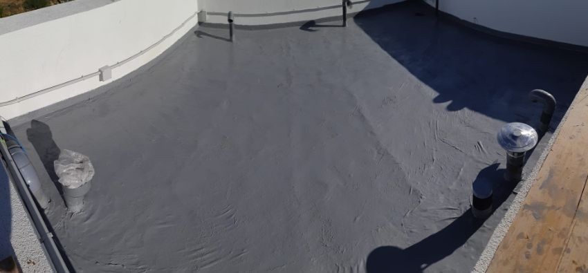 Vista de un techo plano curvo, recientemente recubierto con sellador gris, con paredes blancas y accesorios de metal.