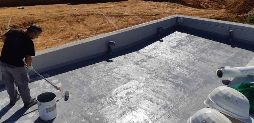 Persona que aplica una capa gris sobre una superficie de hormigón, probablemente para impermeabilizar un contenedor.