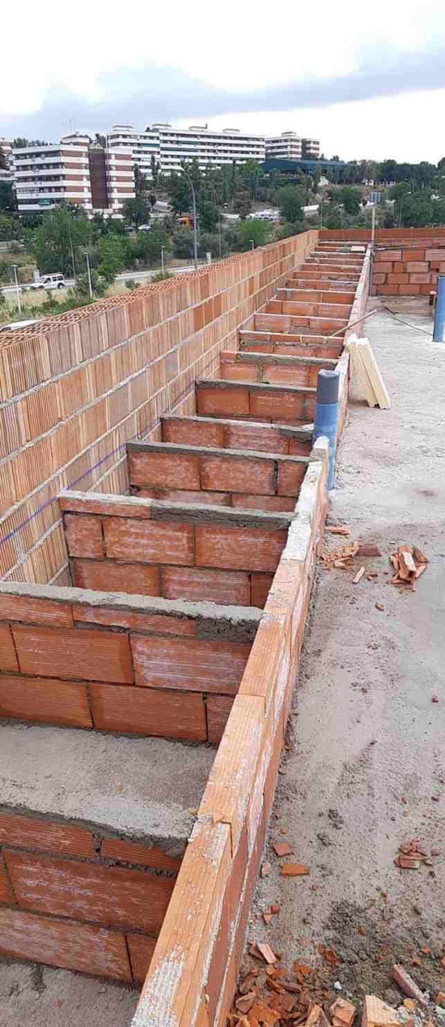 Escaleras de ladrillo en construcción con edificios a lo lejos. Cielo nublado.