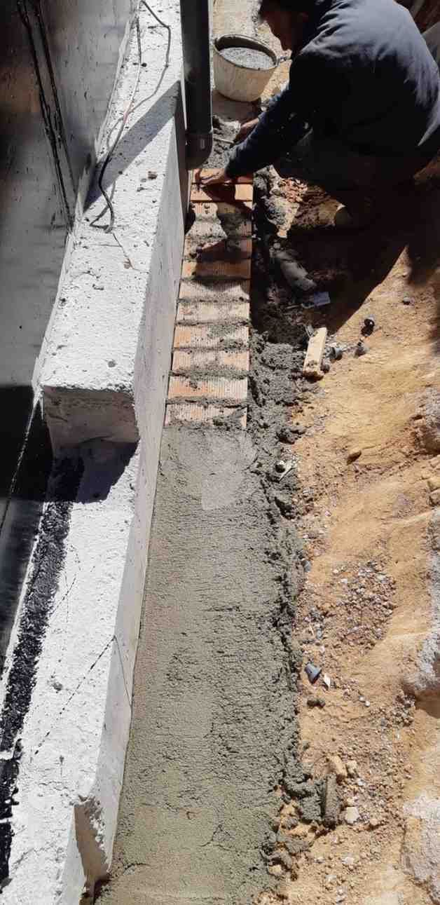 Obrero colocando ladrillos en una zanja junto a un muro de hormigón.