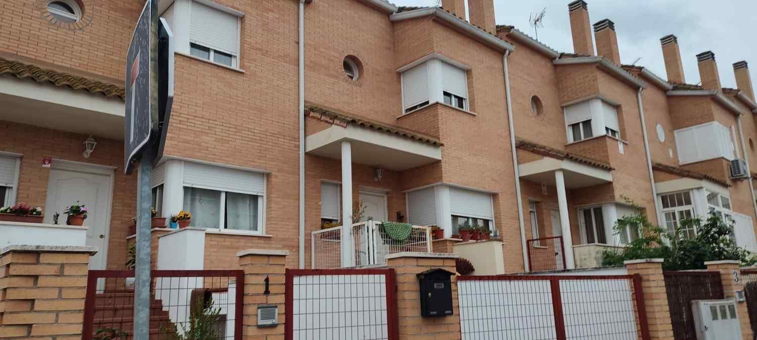 Hilera de casas adosadas de ladrillo con contraventanas blancas y balcones detrás de un muro bajo de ladrillo.