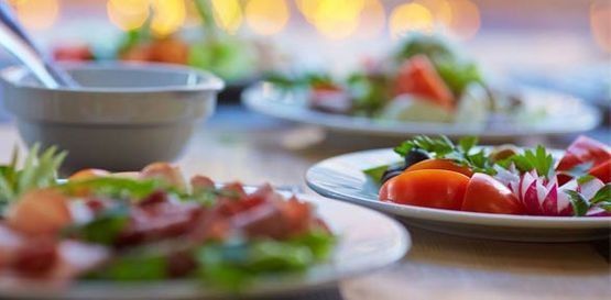 Platos de ensalada fresca y verduras sobre una mesa de comedor con cuencos al fondo.
