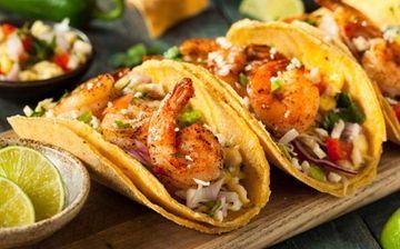 Tres tacos de camarones en una tabla de madera con rodajas de lima y salsa.
