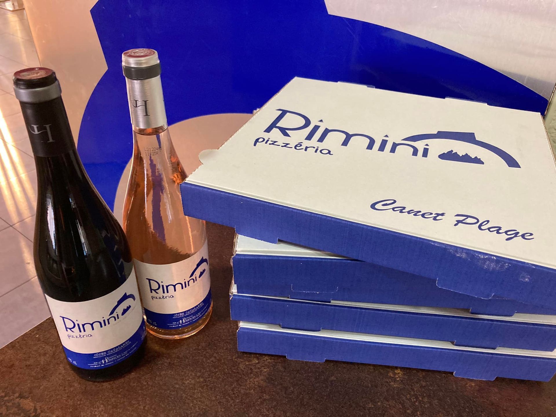 Des boîtes à pizzas empilées et des bouteilles de vin.