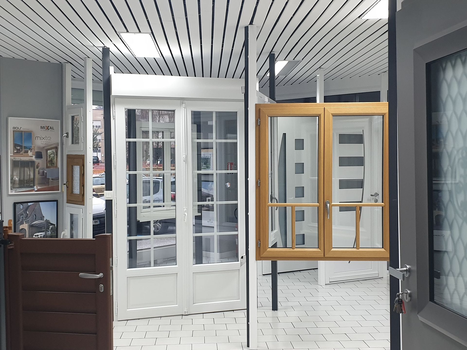 Une salle d'exposition de fenêtres et de portes présente différents styles, notamment une fenêtre en bois et des portes blanches.