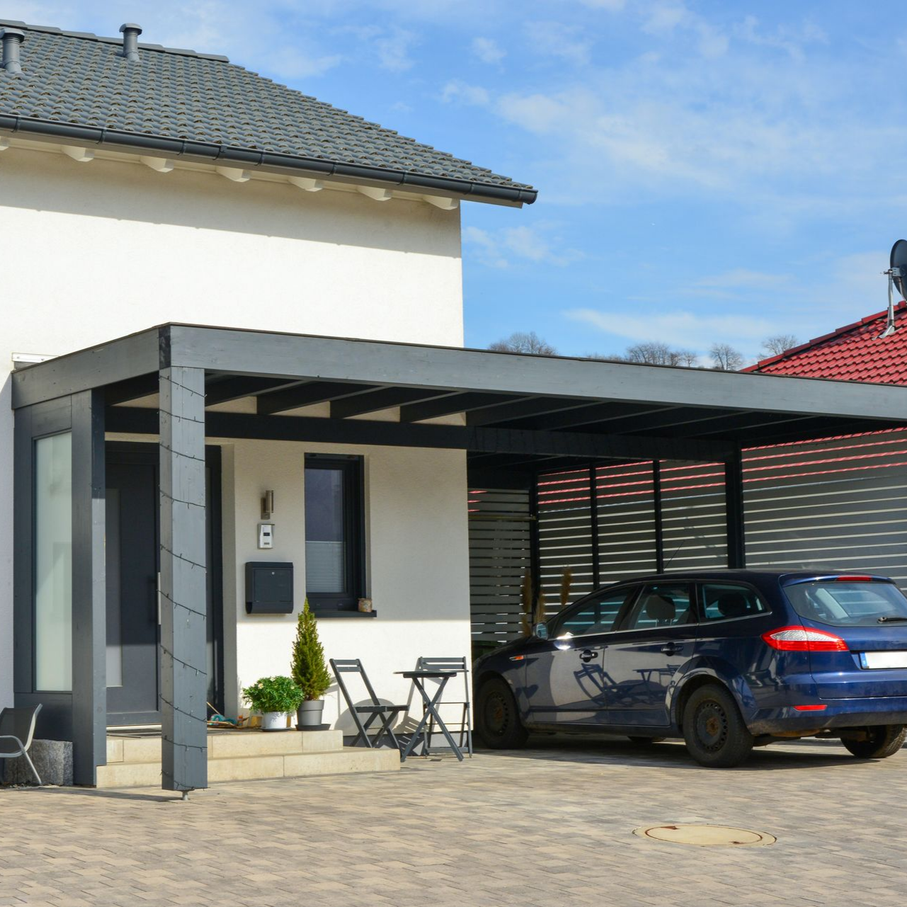 Carport en aluminium adossé à une maison avec une voiture dessous.