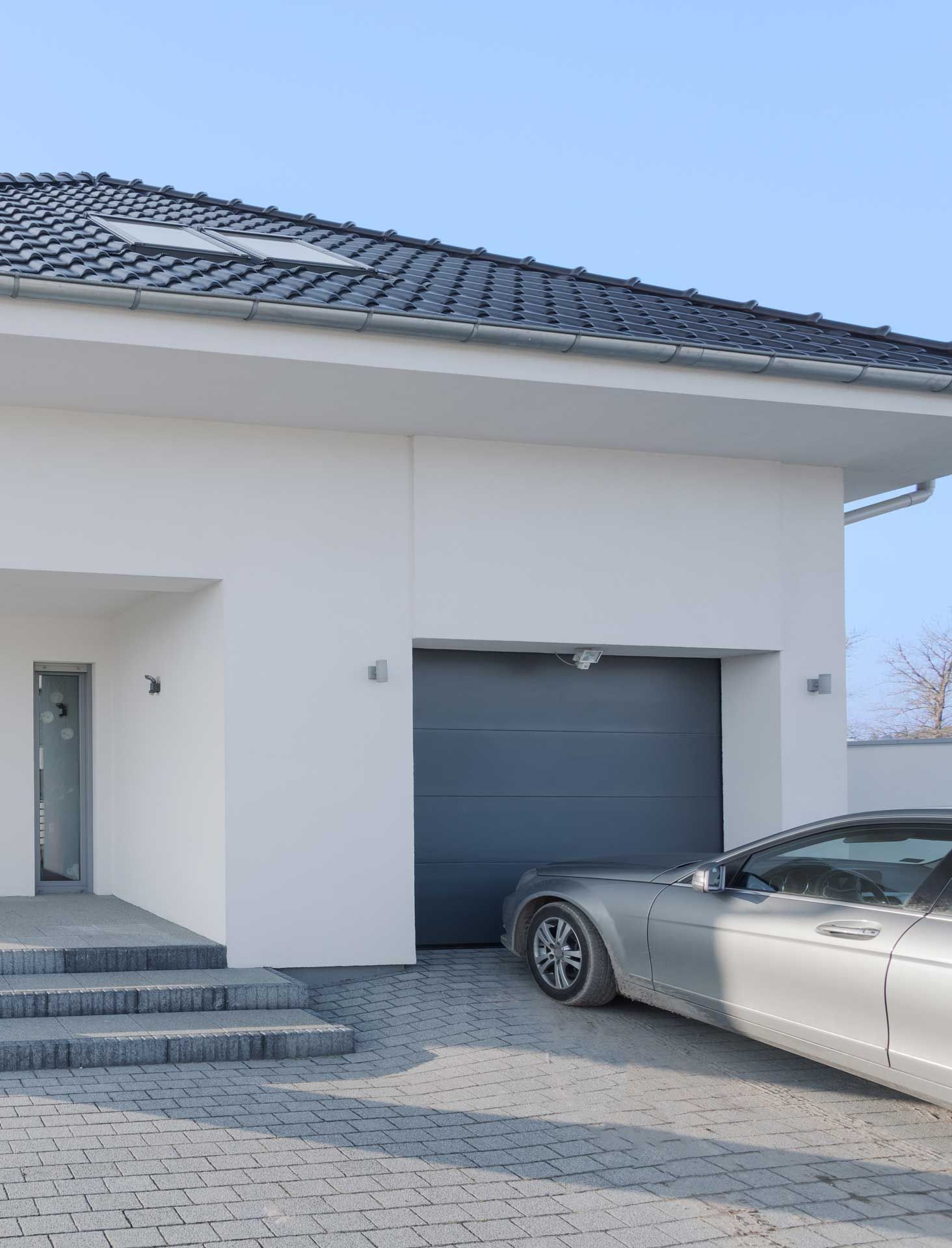 Une voiture grise devant la porte de garage d'une maison.
