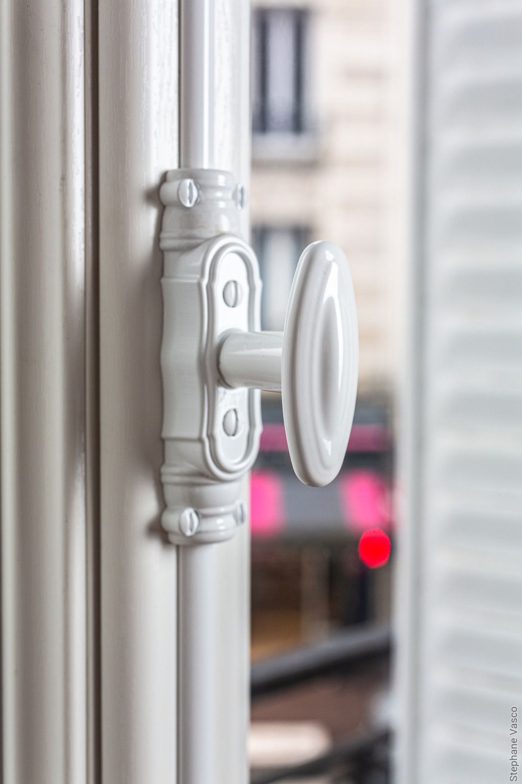 Loquet de fenêtre blanc avec poignée ovale ; fenêtre partiellement ouverte avec fond de ville.