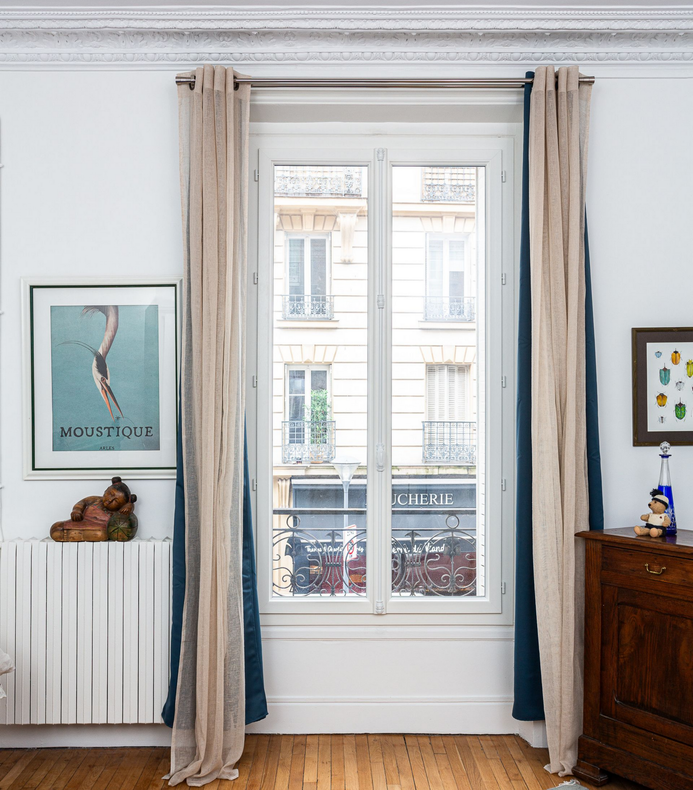 Fenêtre avec rideaux beiges transparents et vue sur une rue.