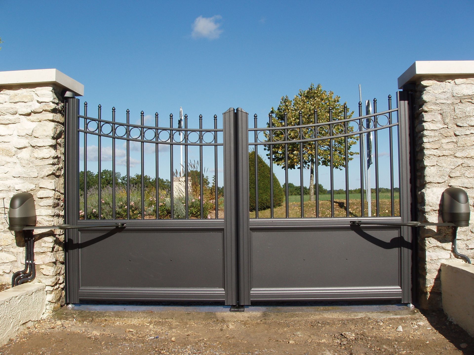 Portails d'allée en métal gris avec ouvre-portes automatiques encastrés dans des piliers en pierre.