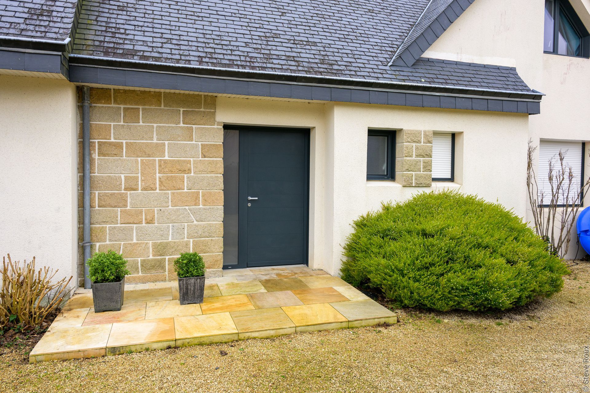 Entrée avec porte grise, mur en pierre et patio en pierre jaune.