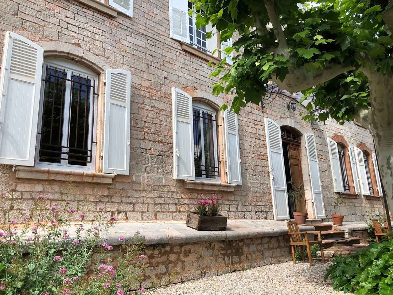 Bâtiment en briques avec volets blancs, fenêtres à barreaux et porche en pierre.