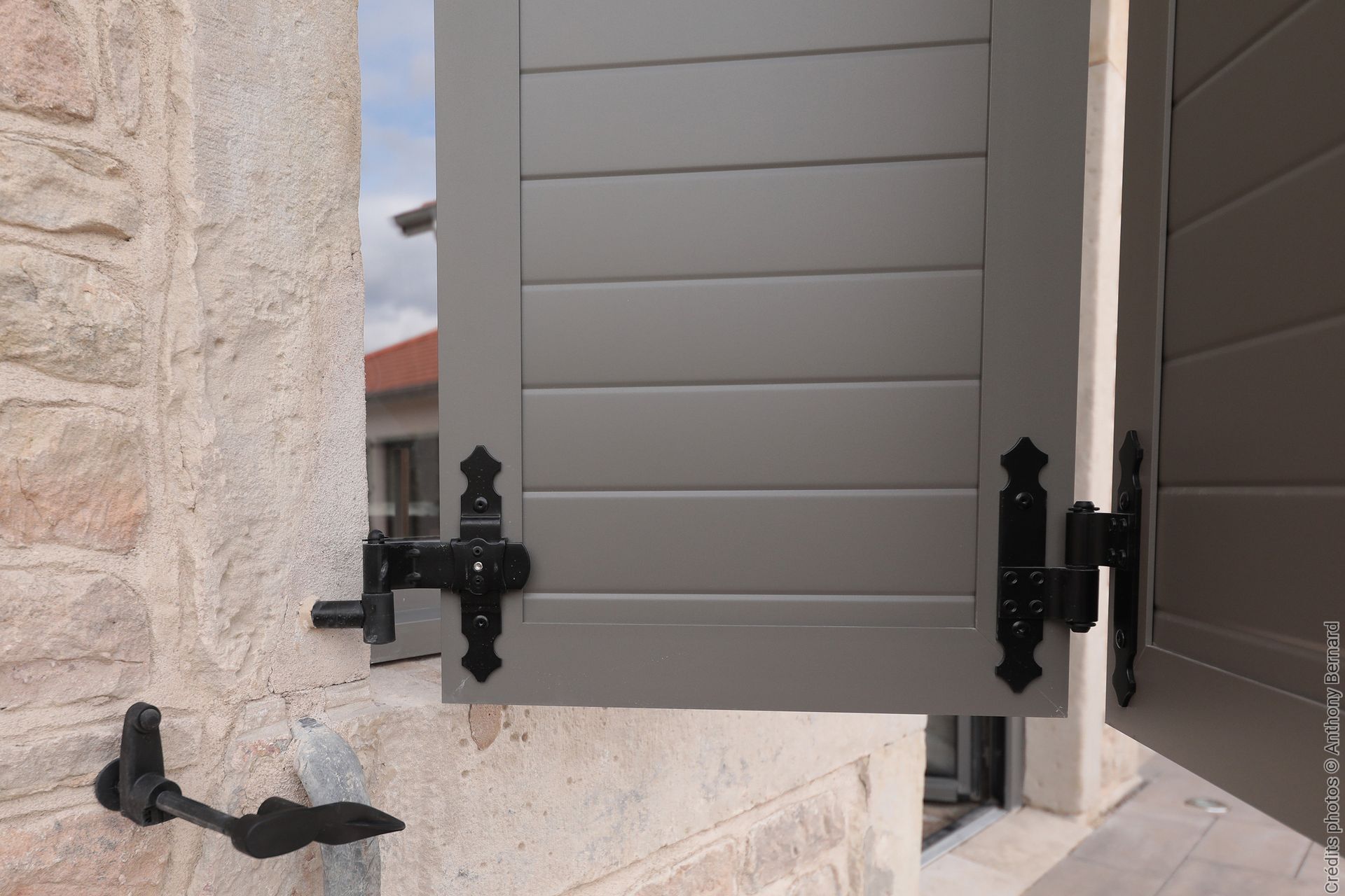 Volets gris avec charnières décoratives noires sur un mur en pierre.