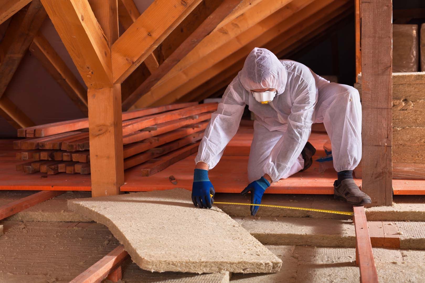 Un homme installe une plaque d'isolant dans des combles.