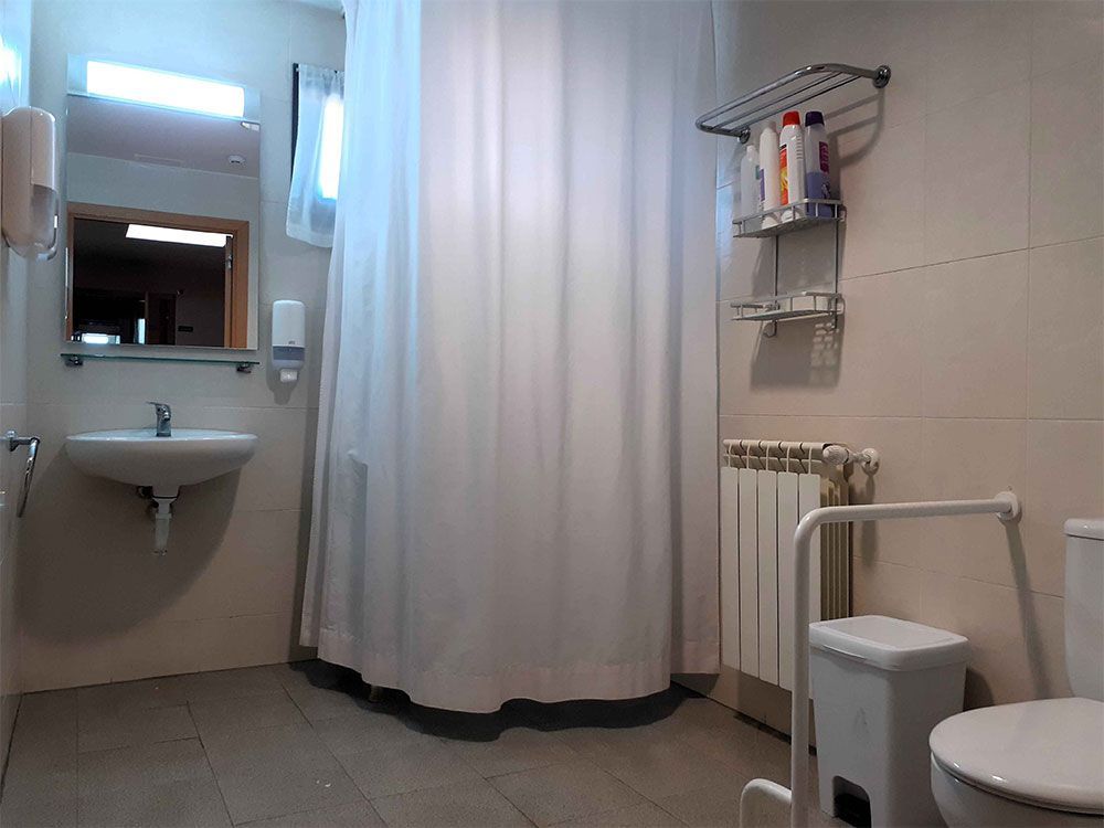 Bany accessible amb cortina de dutxa, lavabo, vàter i barra d'agafada.