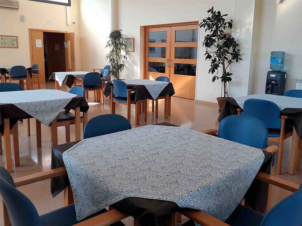 Un menjador escassament moblat amb taules quadrades cobertes amb estovalles estampades i cadires blaves.