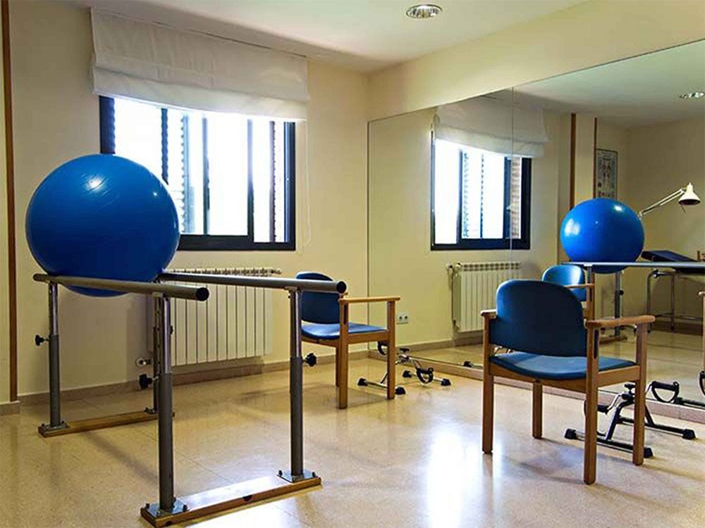 Una sala de fisioteràpia amb equipament d'exercici, com ara una pilota d'exercicis blava i barres paral·leles.