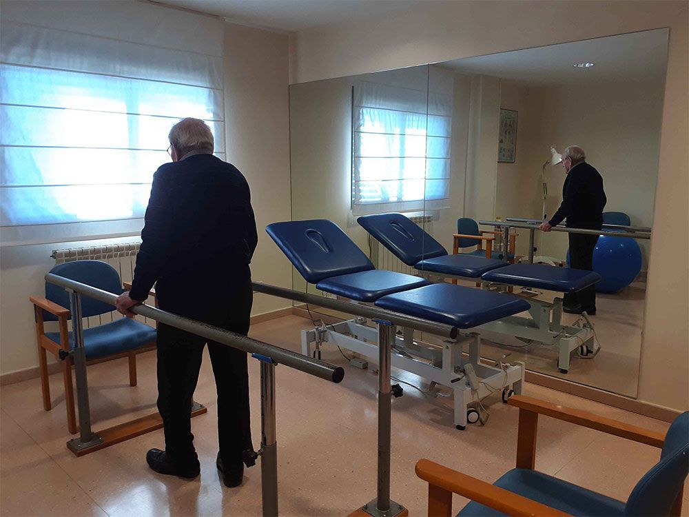 Home utilitzant barres paral·leles per a fisioteràpia en una sala de rehabilitació.