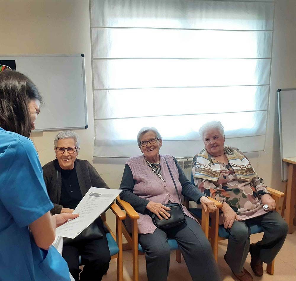 Cuidador hablando con tres personas mayores sentadas en el interior.