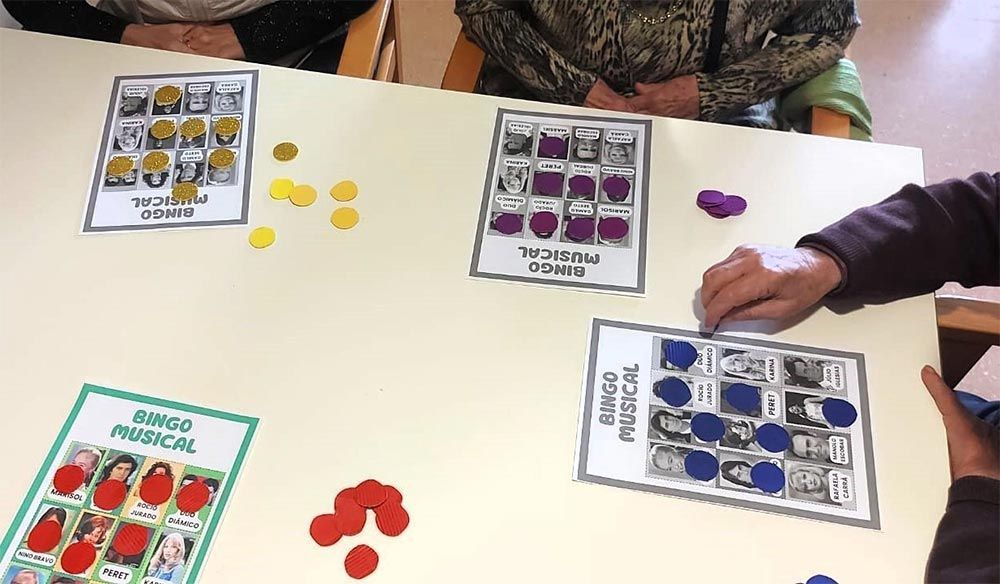 Personas jugando al bingo musical, utilizando cartones y fichas de colores, en una mesa.