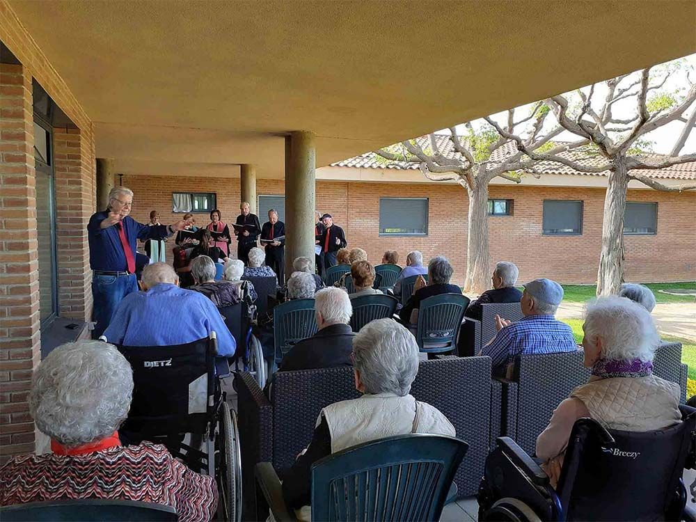 Personas mayores sentadas, viendo una actuación musical al aire libre bajo un área cubierta.