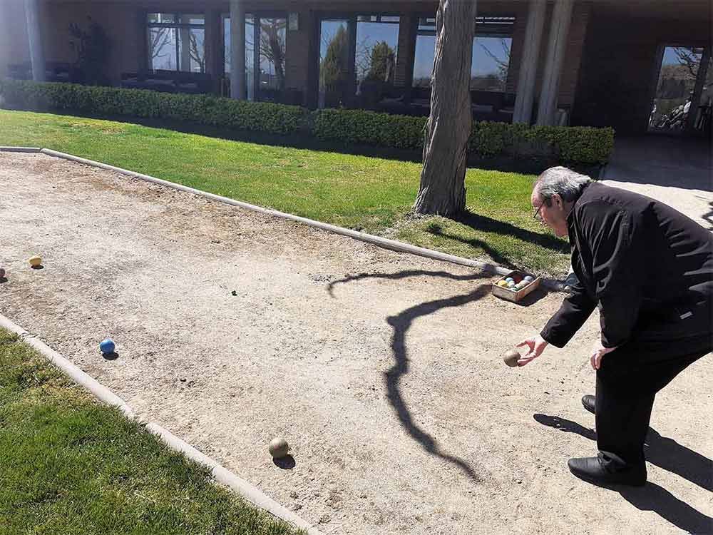 Hombre jugando a la bocha en una cancha de tierra frente a un edificio.