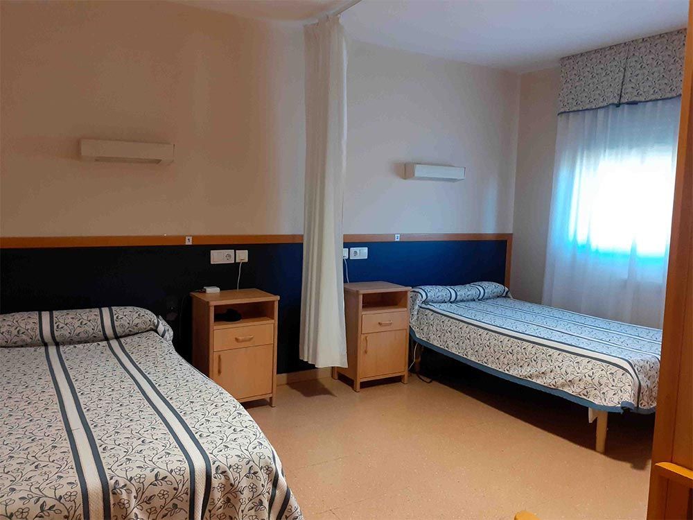 Dos llits individuals en una habitació amb tauletes de nit a joc, decoració blava i blanca i una finestra amb cortines.