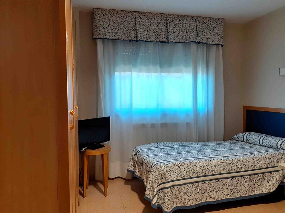 Dormitori amb llit, televisor, armari i finestra amb cortines.