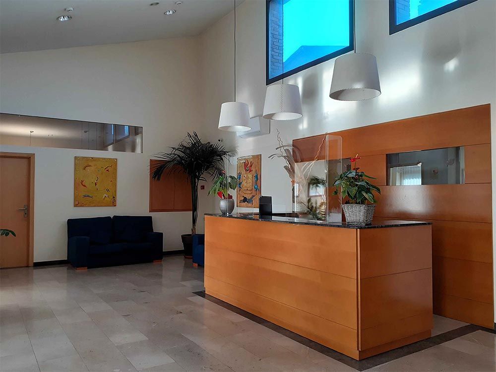 Vestíbul amb un taulell de recepció de fusta, sofà, obres d'art i plantes. Parets blanques i beix, làmpades de sostre.