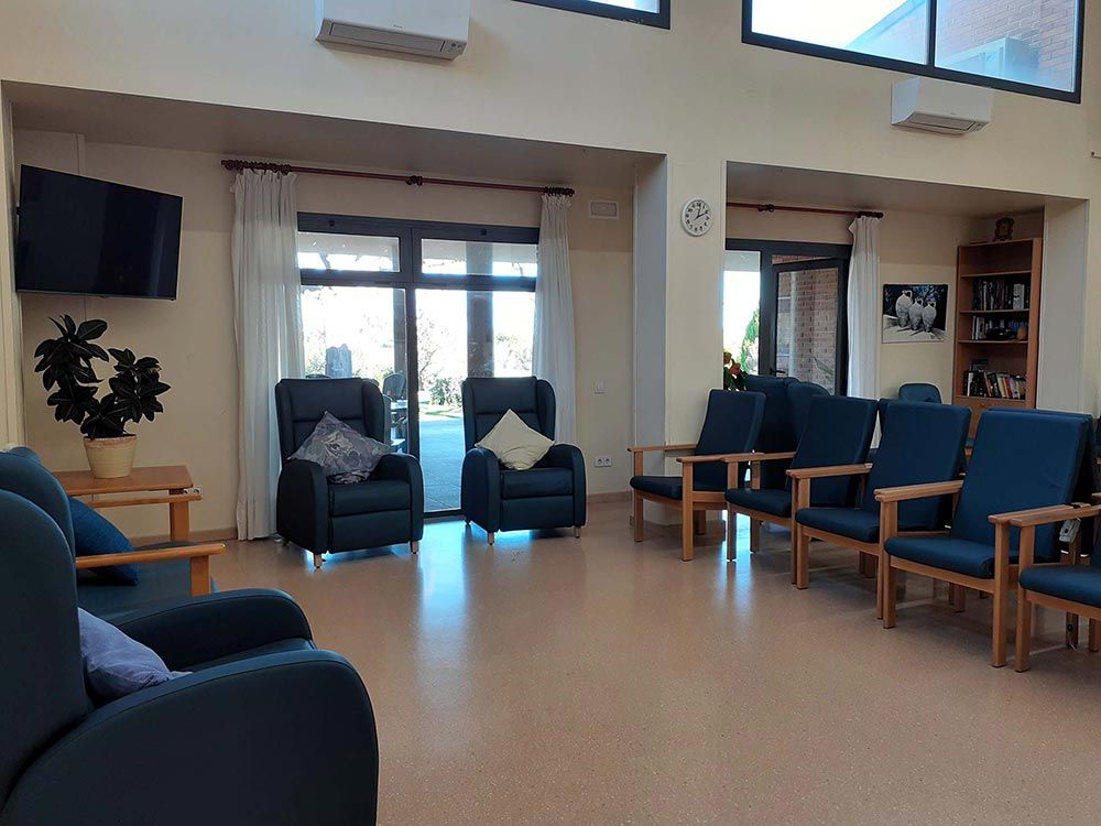 Ampli saló amb diverses butaques i cadires, davant d'una porta de pati. També es veu un televisor i una prestatgeria penjats a la paret.