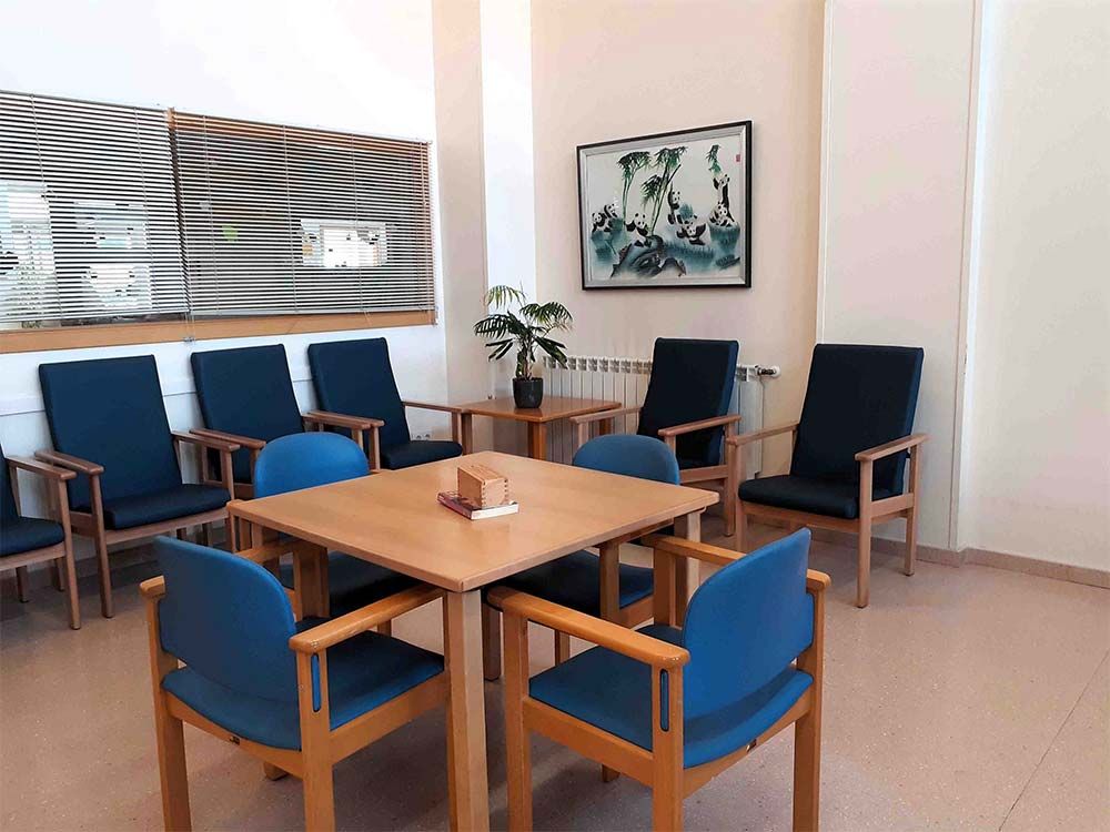 Sala d'espera amb cadires blaves i taules de fusta. Obres d'art i una planta decoren l'espai.