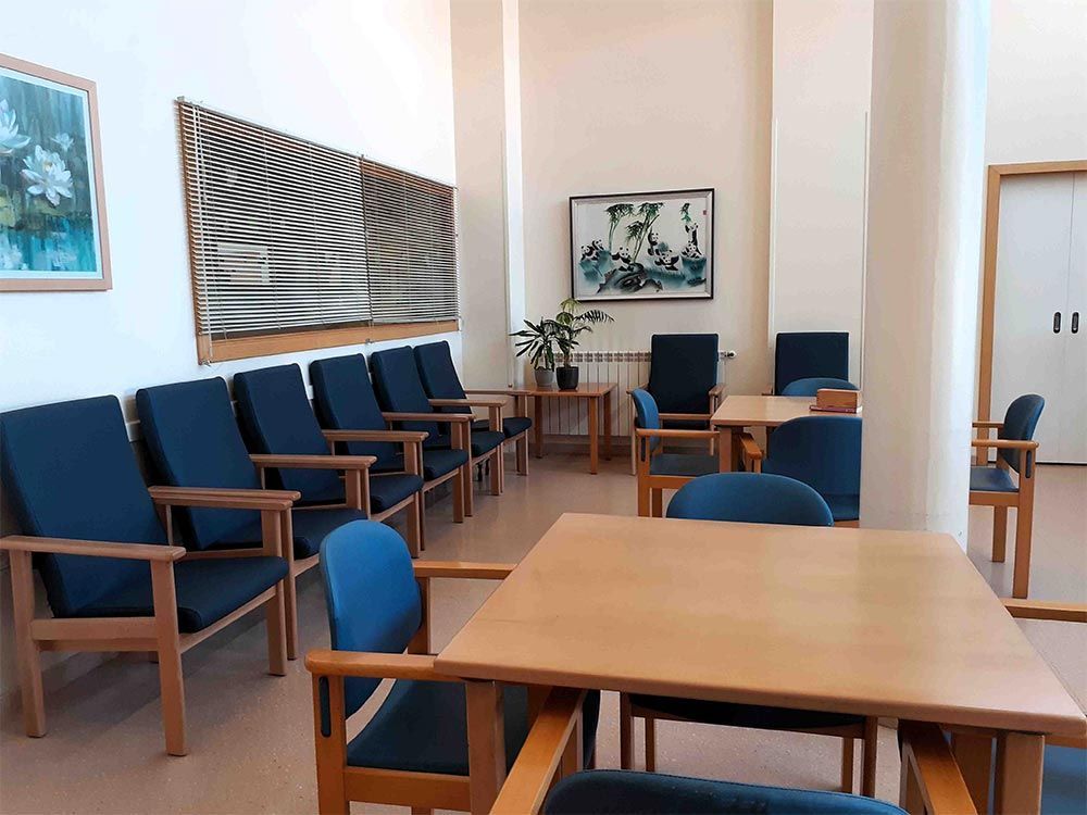 Una sala d'espera amb fileres de cadires i taules blaves. Obres d'art penjades a les parets.