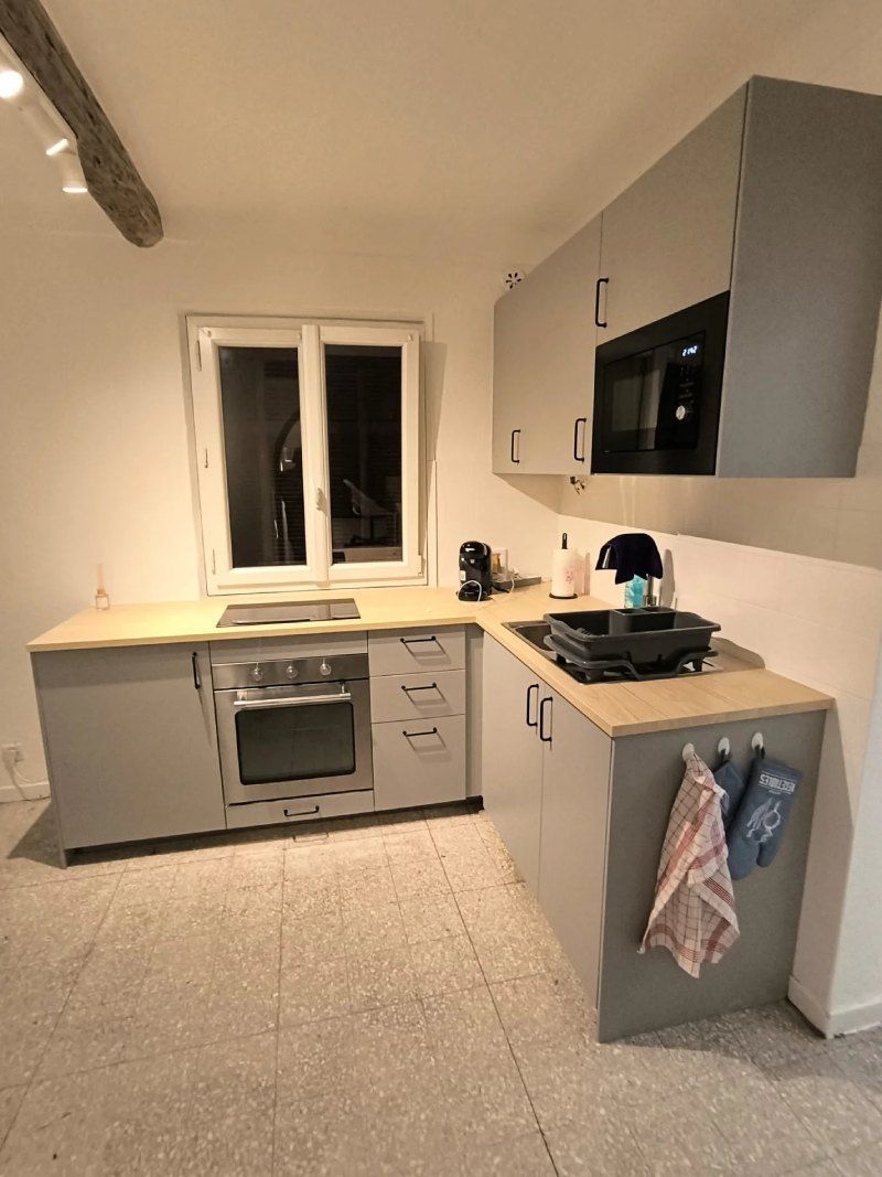 Une cuisine avec des armoires grises, une cuisinière, un évier et une fenêtre.