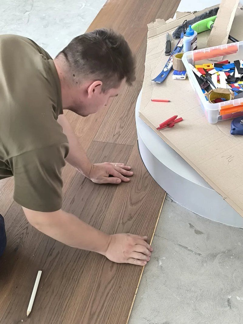 Un homme est agenouillé sur le sol et mesure un morceau de bois.