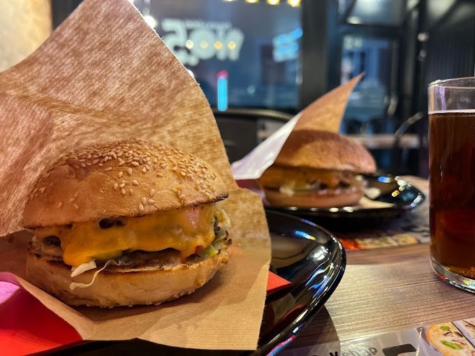Un hamburger emballé dans du papier brun est sur une assiette à côté d'un verre de bière.