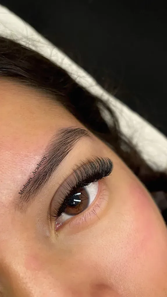 Primer plano de un ojo muy maquillado con largas pestañas postizas y cejas bien definidas.