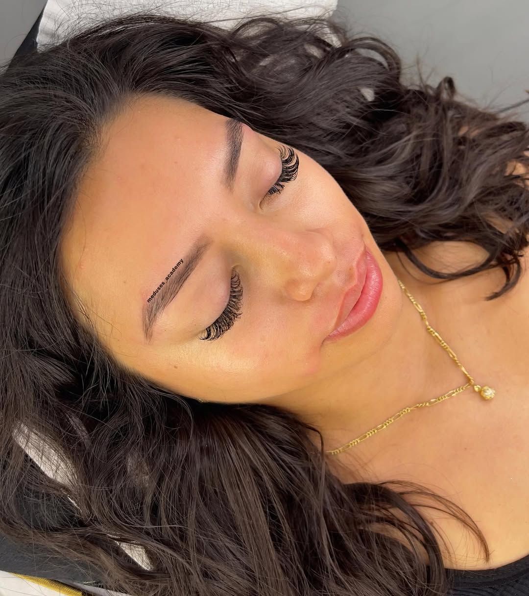 Mujer de cabello largo y oscuro con un collar de oro, recostada sobre una superficie 