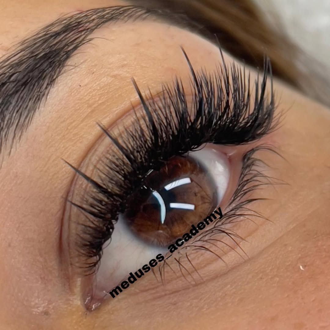 Primer plano de un ojo con pestañas postizas largas y rizadas y un acabado de maquillaje brillante.