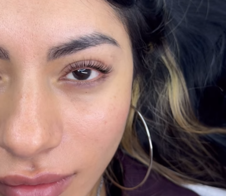 Primer plano del rostro de una mujer con pendiente de aro y cabello oscuro sobre un fondo oscuro.