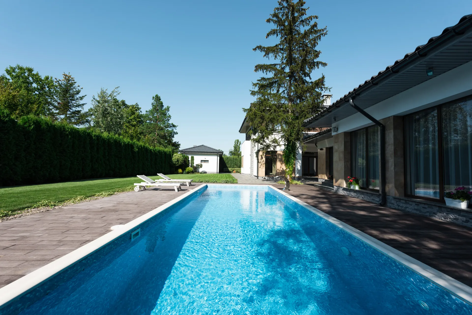 piscina alargada con azulejos azules con suelo de afuera marrón y con césped
