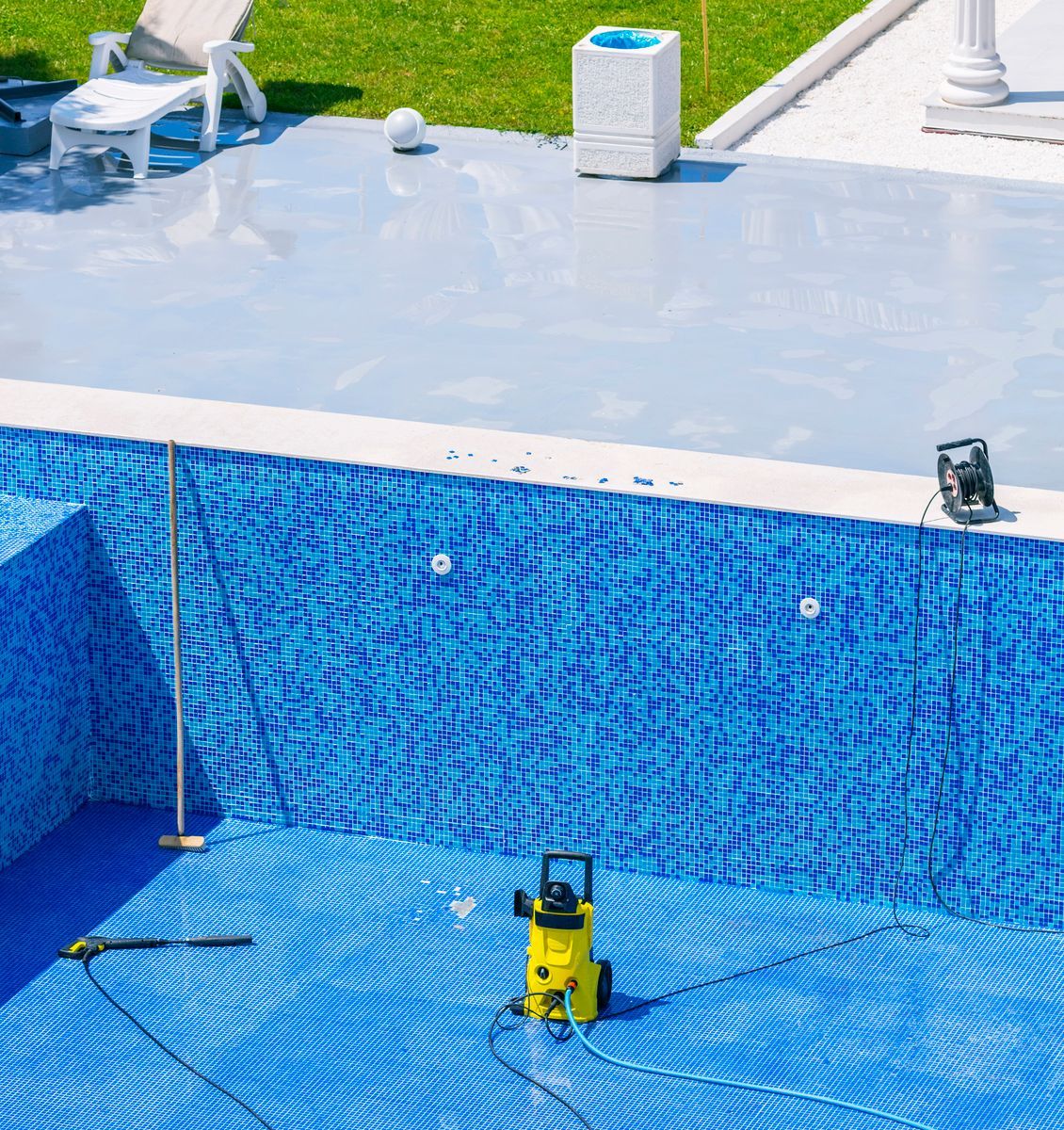 Piscina vacía con azulejos azules claros y oscuros con una maquina para limpiarla